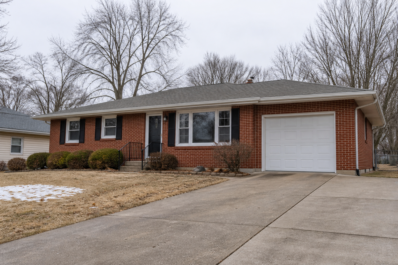 Illustrative brick home with a clear driveway, bare trees and a small patch of snow for winter property-care context.